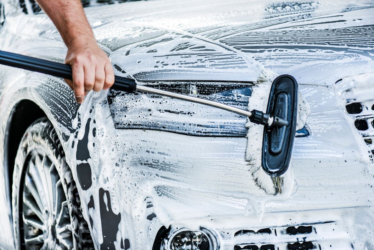 Man washing front bumper and head lights on luxury car at  touchless station with foam and brush. Cleaning details vehicle concept.